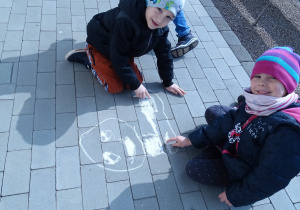 Oluś i Tosia malują Dinka kredą na chodniku